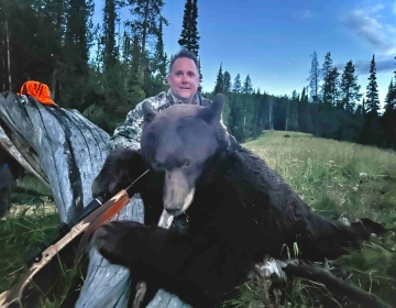 A nonresident Wyoming hunter poses with his black bear draped across a log with his rifle.
